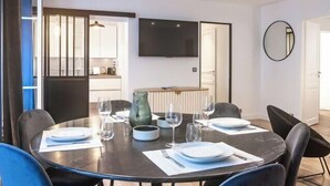 Un coin repas avec une table ronde dressée pour quatre personnes, un téléviseur fixé au mur et un miroir sur le mur.