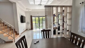 Un espace repas comprenant une grande table, des chaises, un téléviseur et un escalier menant à un autre niveau.
