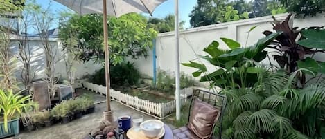 An outdoor patio with a table and chairs, surrounded by potted plants and a white picket fence.