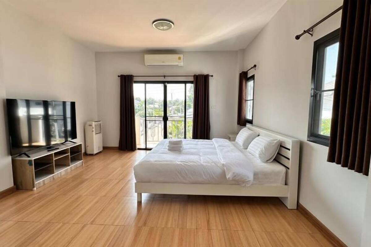 A modern bedroom with a large bed, a flat-screen TV, and an air conditioning unit.