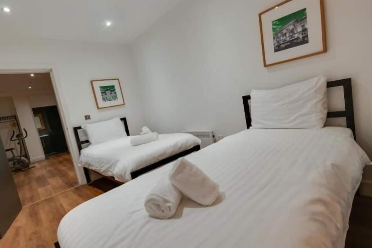A hotel room with two beds, white linens, a framed picture on the wall, and a wooden floor.