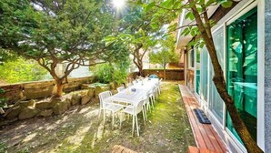 An outdoor dining area with a table and chairs, surrounded by trees and a stone wall. - JT_TEVA (USD) (Seoul)
