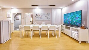 A dining area with a long table, chairs, a television, and a white cabinet. - JT_TEVA (USD) (Seoul)
