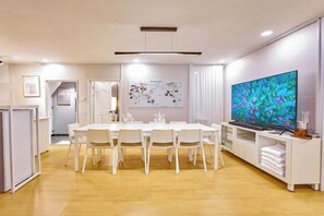 A dining area with a long table, chairs, a television, and a white cabinet. - JT_TEVA (USD) (Seoul)