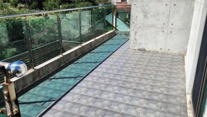 Un balcon doté d’une barrière en verre, d’un sol carrelé et d’un pilier en béton.