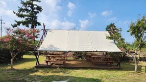 Un espace extérieur abrité, doté de tables de pique-nique, entouré d’arbres et d’une pelouse.