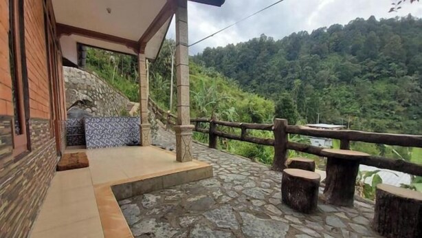 Une terrasse dallée de pierres, avec des tables et des bancs en bois, un escalier en pierre et une vue sur une colline verdoyante.