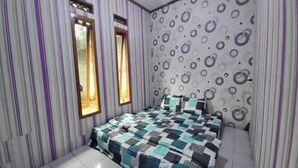 Une chambre avec des murs à rayures, un lit recouvert d’une couvre-lit à motifs et deux fenêtres.