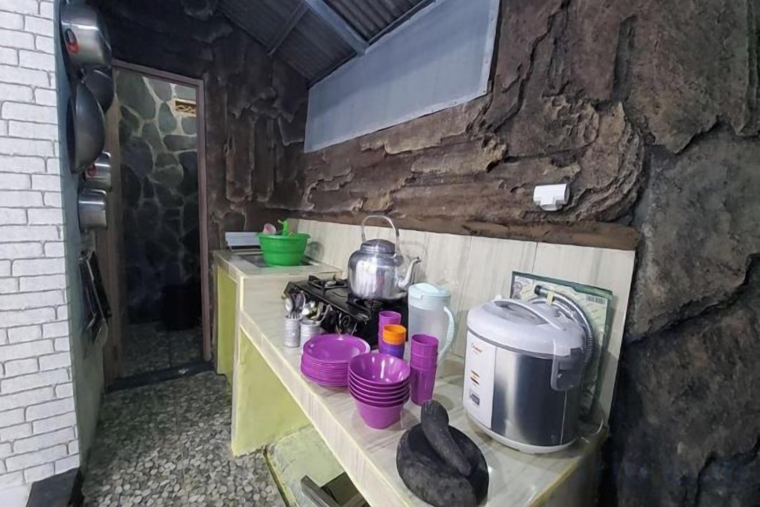 A rustic kitchen with a stone wall, a wooden counter, and various kitchen utensils and containers.