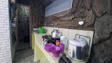 A rustic kitchen with a stone wall, a wooden counter, and various kitchen utensils and containers.
