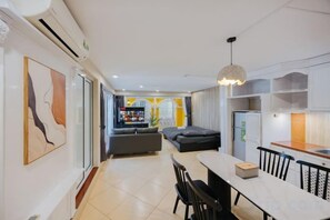 Una sala de estar moderna con un sofá, una mesa de comedor y sillas. Hay una zona de cocina con armarios y un refrigerador.