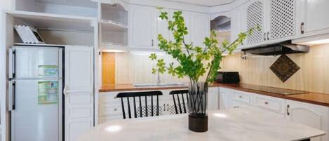A modern kitchen with white cabinetry, a marble countertop, and a central island with chairs.