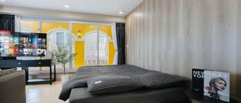 A hotel room with a bed, a small table, a chair, and a view of the outside.