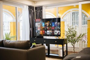 A living room with a flat-screen TV on a stand, a sofa, and a small table with a plant. - VietHOME - 22 Pho Hue - Duplex 602 (Hanoi)