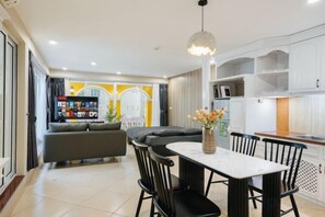 A modern living room with a sofa, dining table, and chairs, a kitchen area with cabinets, and a television. - VietHOME - 22 Pho Hue - Duplex 602 (Hanoi)