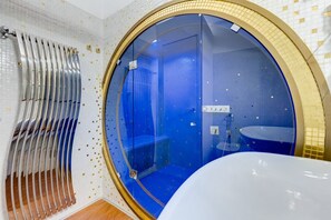 A bathroom with a large circular window, a bathtub, and a shower area.