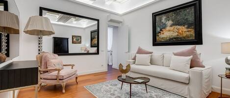 A living room with a white sofa, a pink armchair, a round coffee table, and a large painting on the wall.