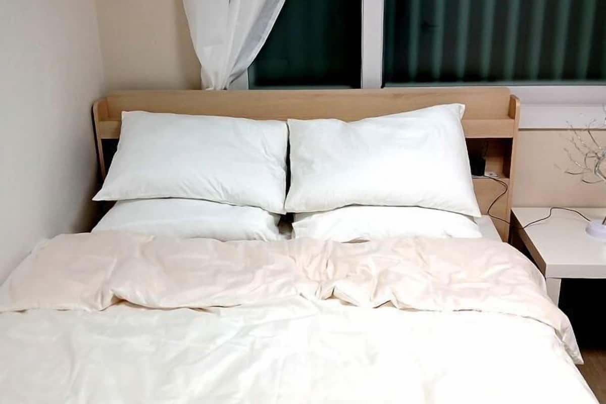 A neatly made bed with white bedding, a wooden headboard, and a bedside table with a lamp.