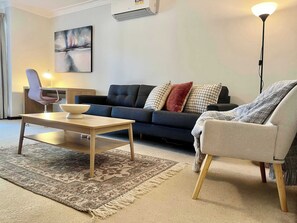 Ein Wohnzimmer mit einer Couch, einem Sessel, einem Couchtisch, einem Teppich und einem Gemälde an der Wand.