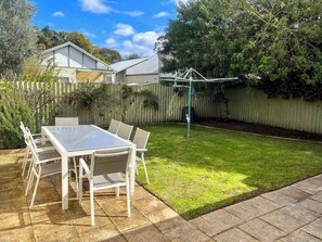 Ein Garten mit einer Terrassentischgruppe, einem Holzzaun und einem Rasen.