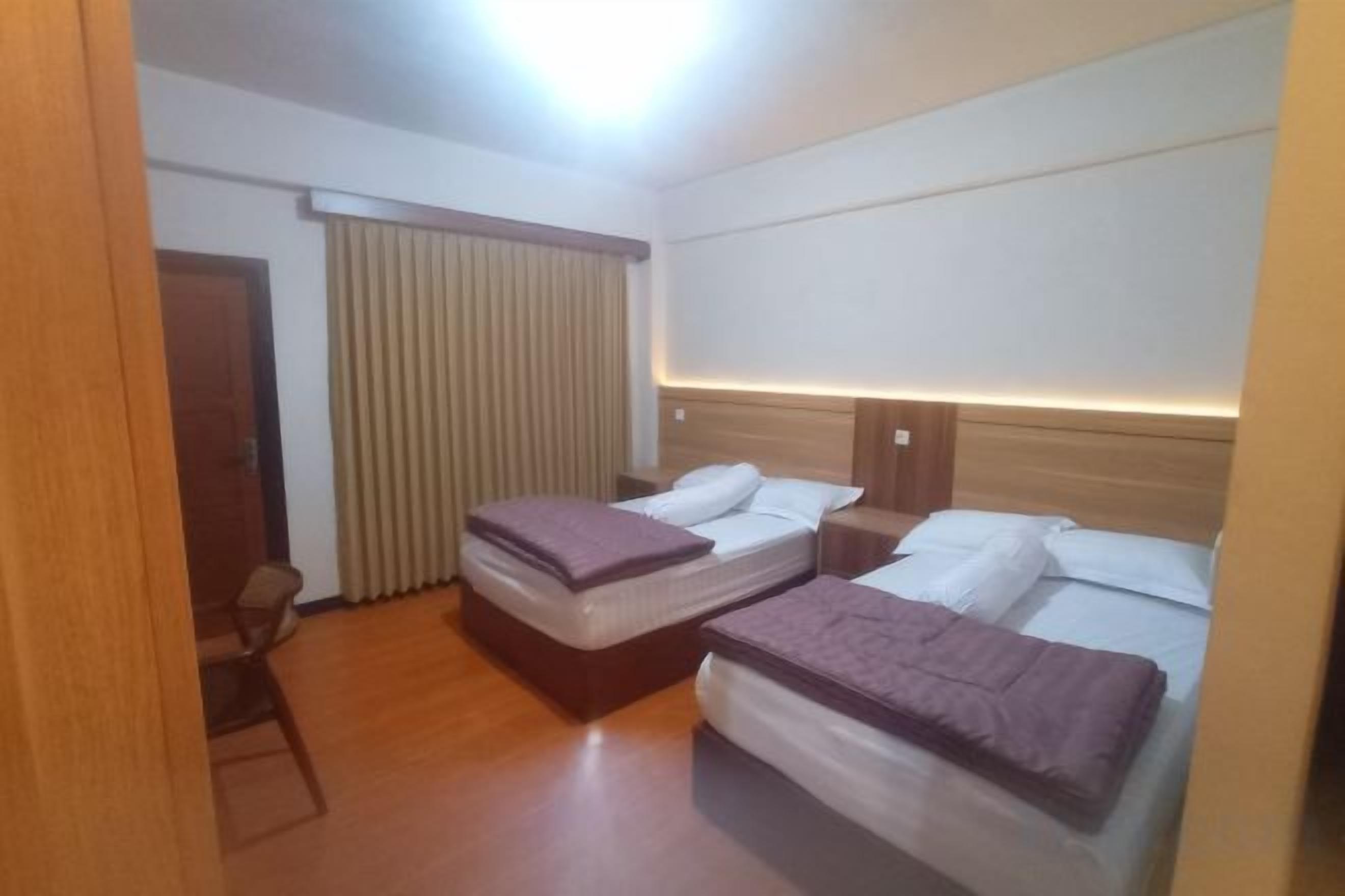 A hotel room with two beds, a desk, a chair, and a window with curtains.