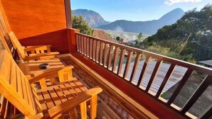 Una terraza de madera con sillas y una mesa, con vistas a un paisaje montañoso.