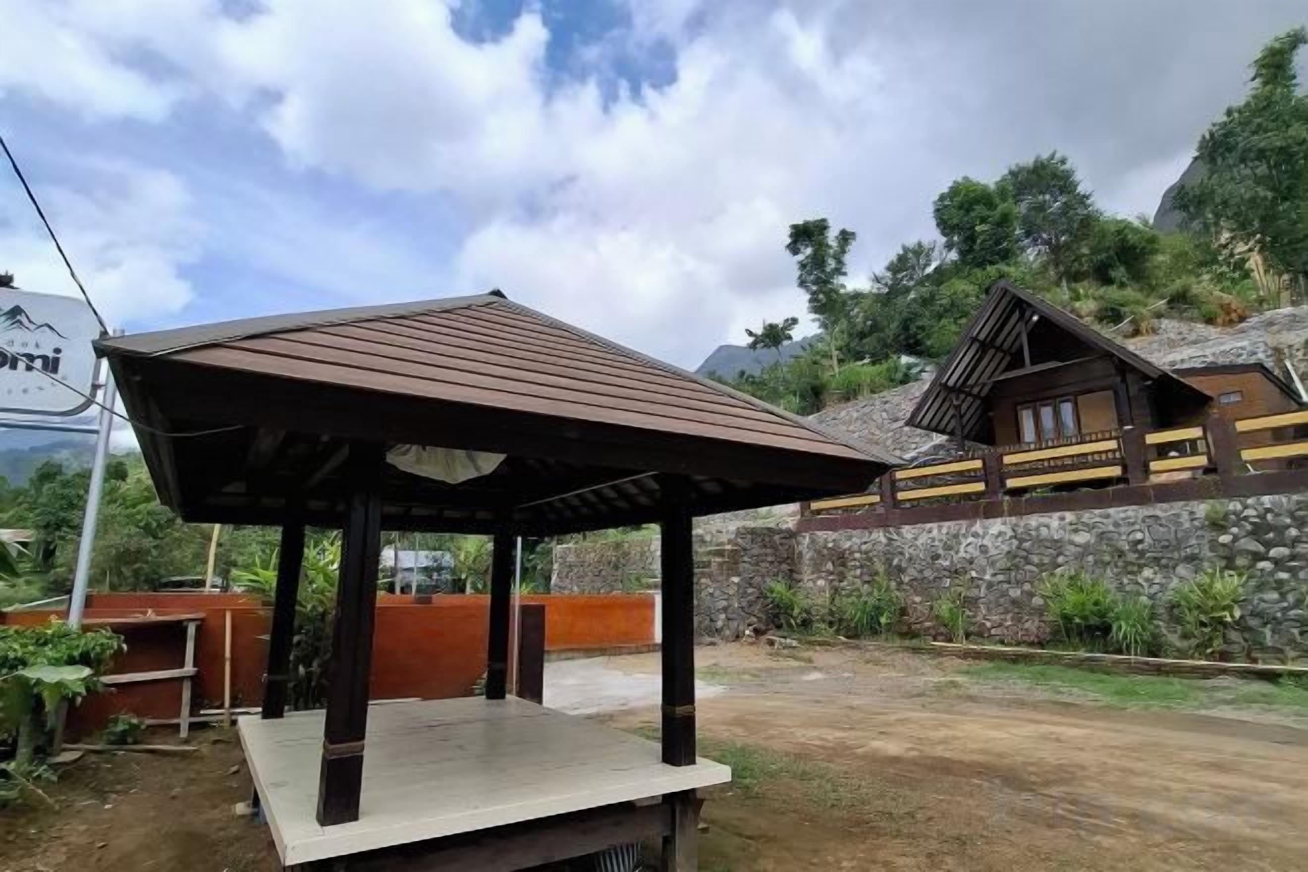 A wooden gazebo with a tiled floor, a stone wall, and a mountain backdrop.