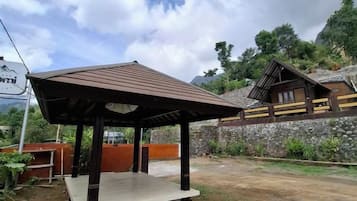 A wooden gazebo with a tiled floor, a stone wall, and a mountain backdrop.