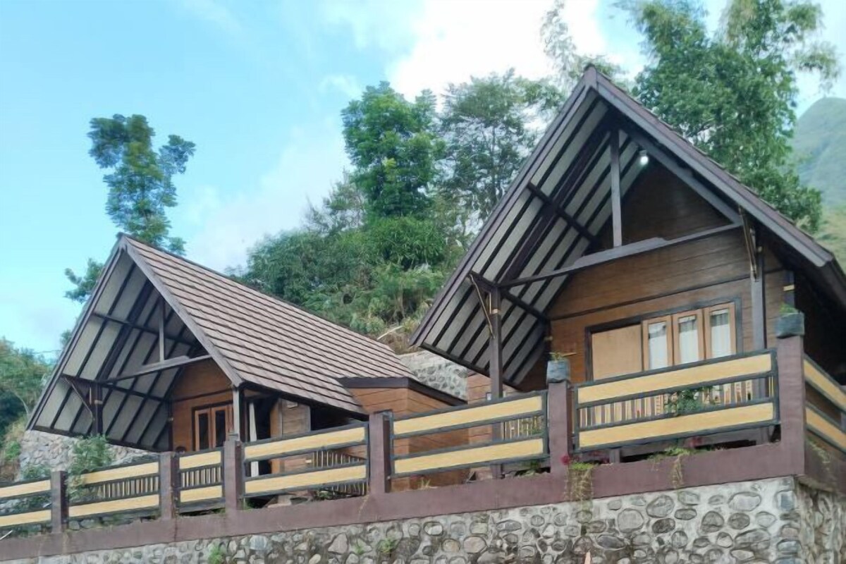Una cabaña en la ladera con cimientos de piedra, fachada de madera y un balcón con barandilla.