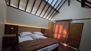 Un dormitorio con tragaluz, una cama con manta marrón, un armario y una puerta con cortinas.