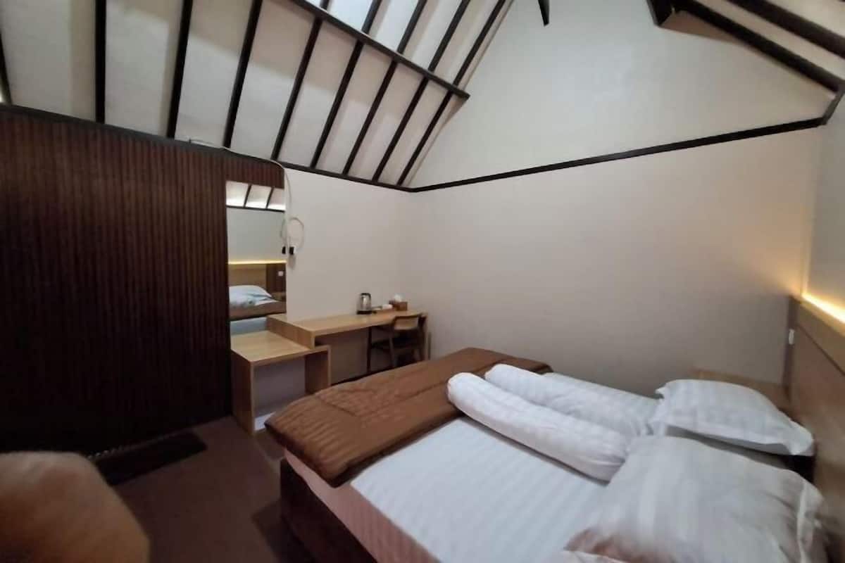 Une chambre d’hôtel de taille réduite, comprenant un lit, un bureau, une chaise et un miroir.