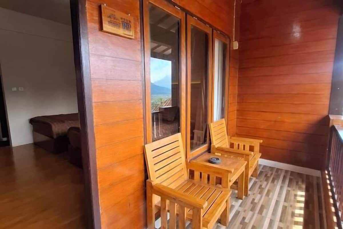 Une pièce au plancher de bois, dotée d’une porte-fenêtre coulissante qui donne sur un balcon où se trouvent deux chaises en bois et une petite table.