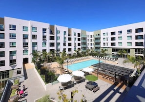 A modern hotel with a rooftop pool, outdoor seating, and palm trees.