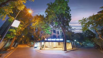 A street view at dusk with a hotel entrance, trees, and streetlights.
