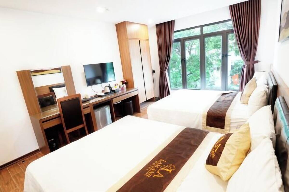 A hotel room with two beds, a desk with a TV, and a window with curtains.
