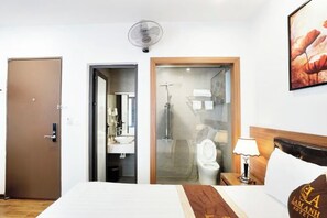 A hotel room with a bed, a bedside table with a lamp, a wooden headboard, a door, and a shower area visible through a glass door. - Lam Anh Hotel 1 Phap Van Hoang Mai (Hanoi)