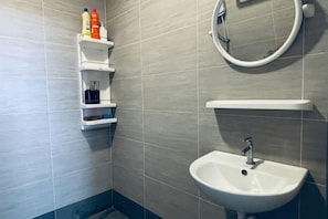 Kylpyhuone, jossa on valkoinen pesuallas, peili ja hylly, jossa on hygieniatuotteita.