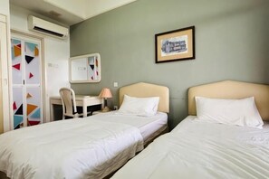 Ein Hotelzimmer mit zwei Betten, einem Schreibtisch, einem Stuhl, einem Spiegel und einem gerahmten Bild an der Wand.