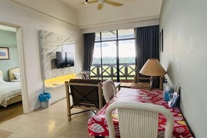 Ein Hotelzimmer mit Bett, Schreibtisch, Stuhl, Fernseher, einem Fenster mit Vorhängen und einem Balkon.