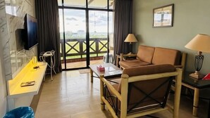 Camera d'albergo con divano, scrivania, televisore, lampada e vista panoramica attraverso una porta vetrata.