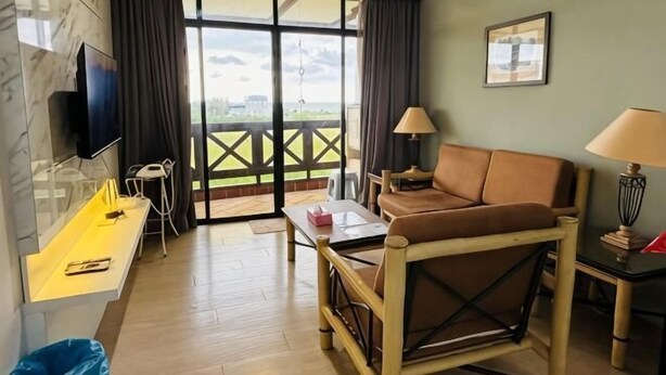 A hotel room with a sofa, a desk, a TV, a lamp, and a view through a glass door. - Heart of City Seaside view Mahkota Costa (Melaka)