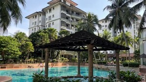 A pool area with a pergola, palm trees, and a multi-story building in the background. - Heart of City Seaside view Mahkota Costa (Melaka)