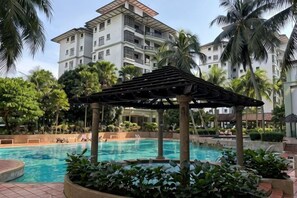 Ein Poolbereich mit einer Pergola, Palmen und einem mehrstöckigen Gebäude im Hintergrund.