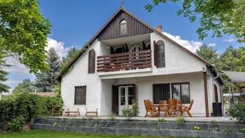 A two-story house with a balcony, a front porch with chairs, and a well-maintained lawn.