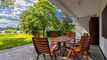 An outdoor patio with a table and chairs, a view of a green landscape, and a tree.
