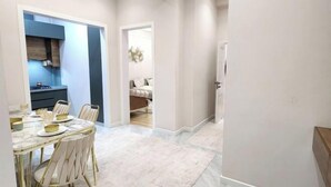 A modern interior with a dining area featuring a marble table and gold chairs, a kitchen with blue cabinets, and a hallway leading to a bedroom. - Apartment Kazahstan in Tashkent (Tashkent)