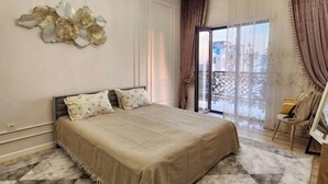 A bedroom with a large bed, a chandelier, a view through a glass door, and a chair by the window. - Apartment Kazahstan in Tashkent (Tashkent)