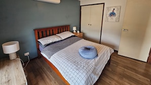 A bedroom with a bed, a nightstand, a lamp, an air conditioner, a ceiling fan, and a wardrobe. - Charming 3-bedroom House in Meadow Heights - Perfect Family Retreat (Melbourne)