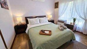 Habitación de hotel con cama, lámparas de noche, ventana con cortinas, mesita de noche con lámpara y aire acondicionado instalado en la pared.