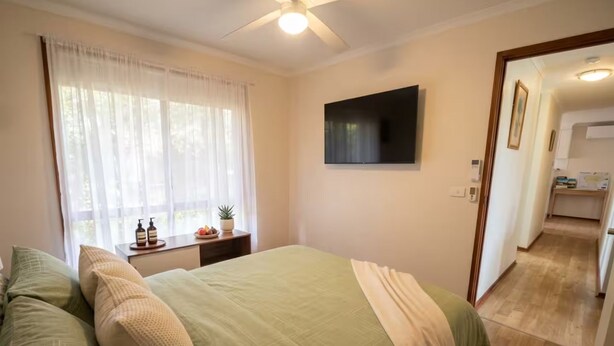 Un dormitorio con una cama, televisor, ventana con cortinas y un pasillo que conduce a un baño.